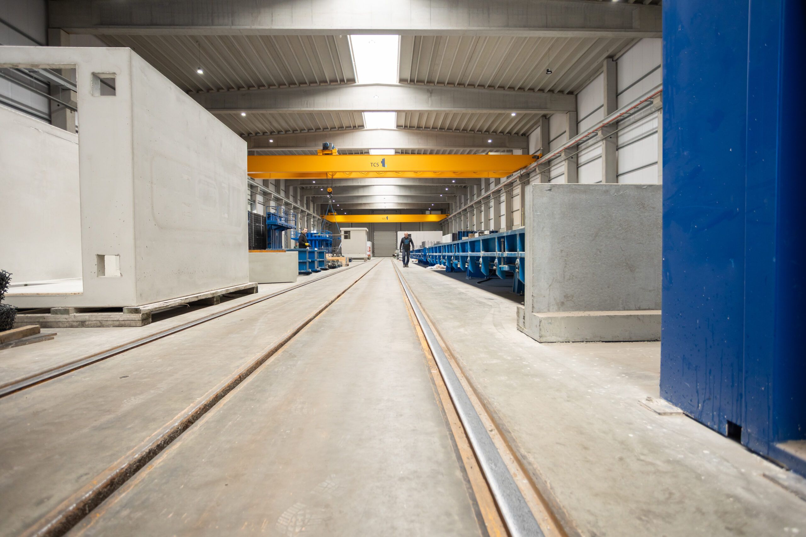 Een medewerker van Webeco begeleidt nauwkeurig de assemblage van prefab betonelementen in een moderne productiehal.

